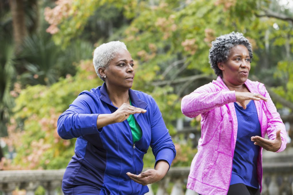 Two senior African American women, doing tai chi exercises at the park.